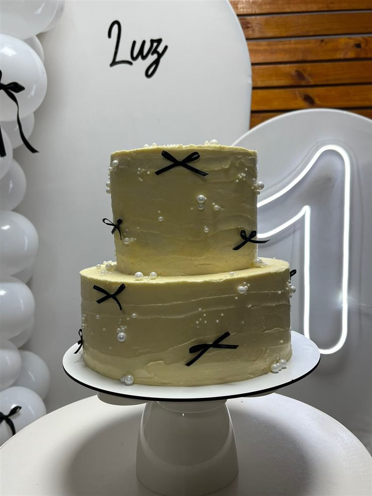 Torta de cumpleaños crema con moños negros y perlas